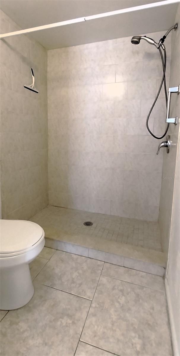 bathroom with tile patterned flooring, a tile shower, and toilet