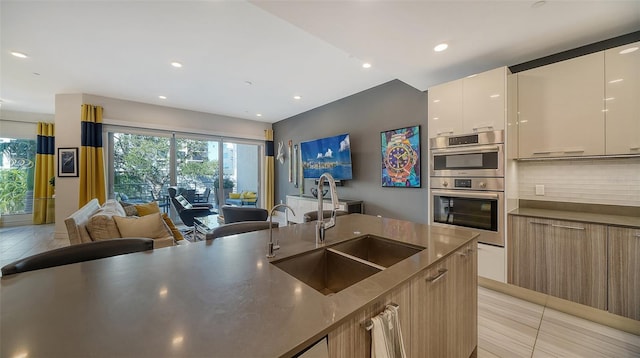 kitchen with tasteful backsplash, double oven, sink, light brown cabinets, and light tile patterned floors