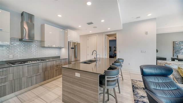 kitchen with sink, stainless steel appliances, wall chimney range hood, a breakfast bar area, and white cabinets