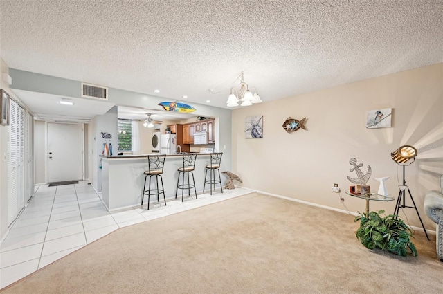 kitchen featuring kitchen peninsula, light colored carpet, a textured ceiling, white appliances, and a breakfast bar area