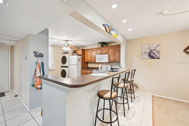 kitchen with a breakfast bar, white appliances, kitchen peninsula, and stacked washer / drying machine