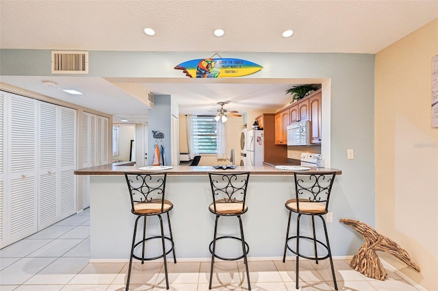 kitchen with a kitchen bar, kitchen peninsula, light tile patterned flooring, and white appliances