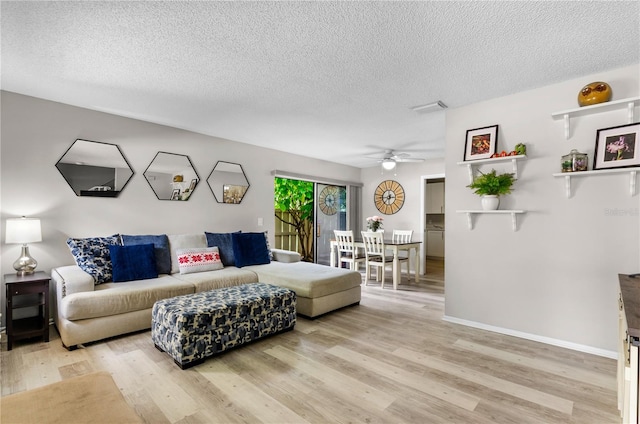 living area featuring a textured ceiling, ceiling fan, light wood-style flooring, visible vents, and baseboards