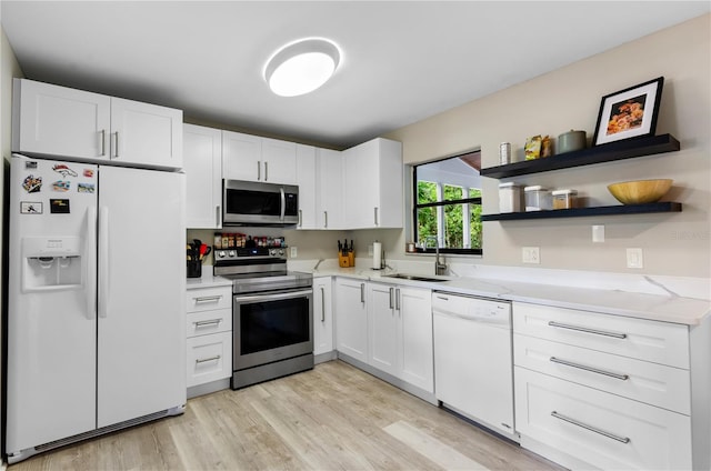 kitchen with appliances with stainless steel finishes, sink, white cabinets, light stone countertops, and light wood-type flooring