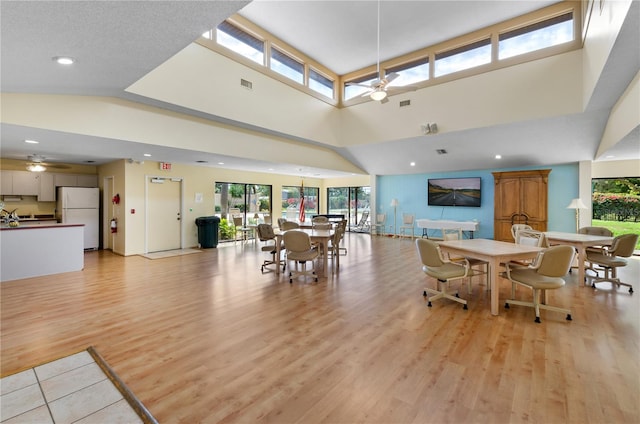 dining room with light hardwood / wood-style flooring, ceiling fan, and a high ceiling