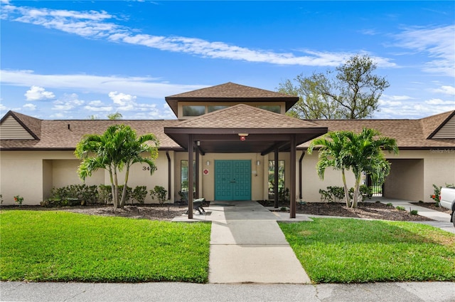 view of front of home with a front lawn, roof with shingles, and stucco siding