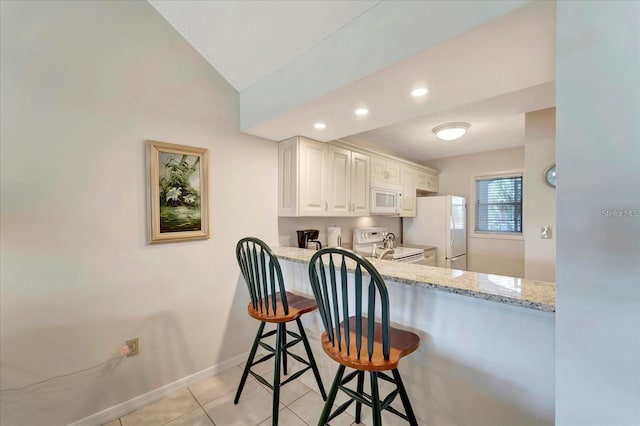 kitchen featuring light tile patterned floors, white appliances, sink, light stone counters, and a kitchen bar