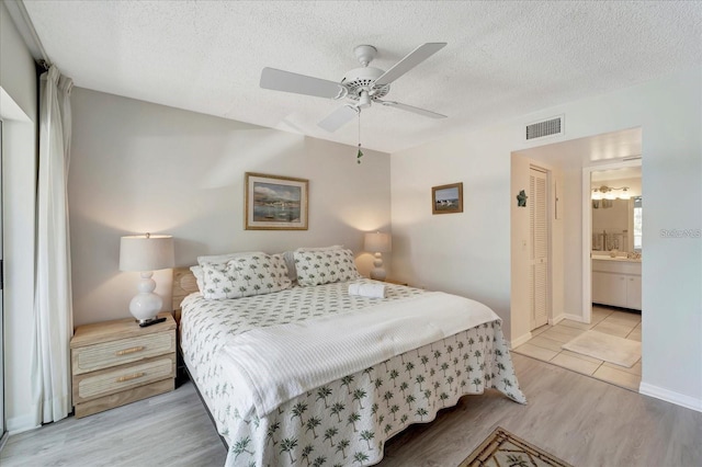 bedroom with ensuite bathroom, ceiling fan, light hardwood / wood-style floors, a textured ceiling, and a closet