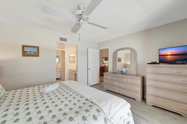 bedroom featuring ceiling fan, connected bathroom, light hardwood / wood-style floors, and a textured ceiling