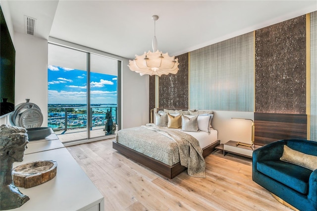 bedroom featuring access to outside, light hardwood / wood-style flooring, expansive windows, and a chandelier