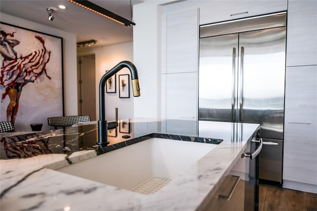 kitchen featuring built in fridge, dark hardwood / wood-style floors, light stone counters, and sink