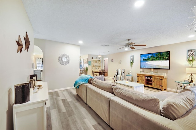 living room with light wood-type flooring, a textured ceiling, and ceiling fan