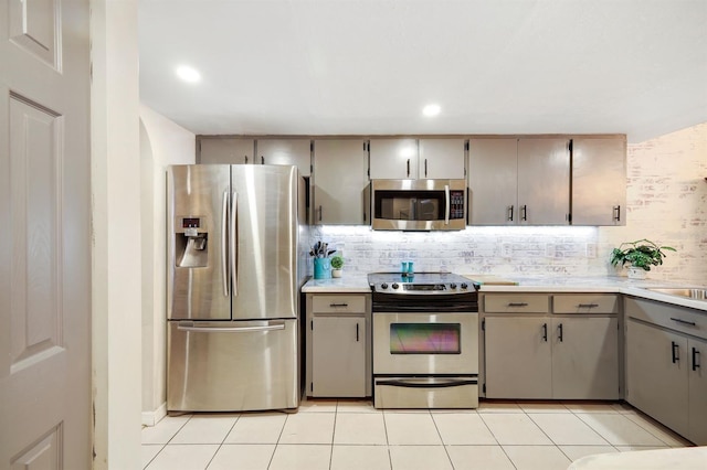 kitchen with gray cabinetry, decorative backsplash, light tile patterned flooring, and appliances with stainless steel finishes