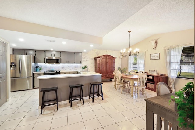 kitchen with gray cabinetry, tasteful backsplash, vaulted ceiling, light tile patterned floors, and appliances with stainless steel finishes