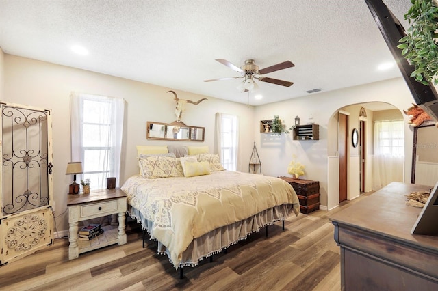 bedroom featuring ceiling fan, wood-type flooring, a textured ceiling, and multiple windows