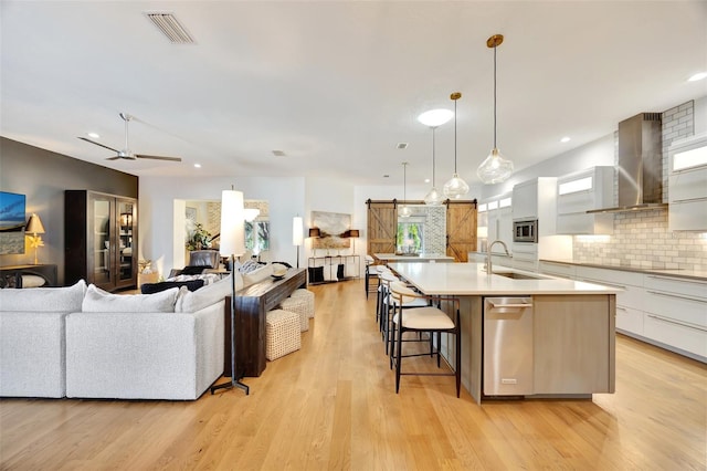 kitchen featuring pendant lighting, sink, wall chimney exhaust hood, a barn door, and white cabinetry