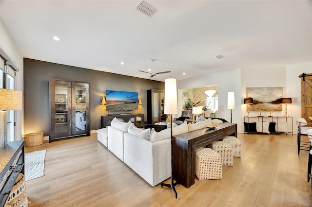 living room featuring ceiling fan, a barn door, and light hardwood / wood-style flooring