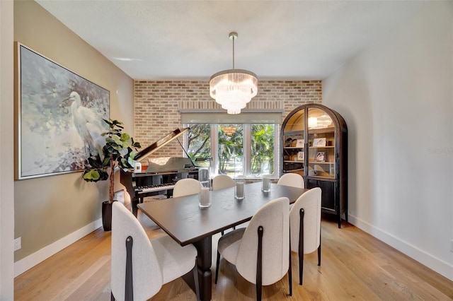 dining area featuring light wood-type flooring, brick wall, and a chandelier