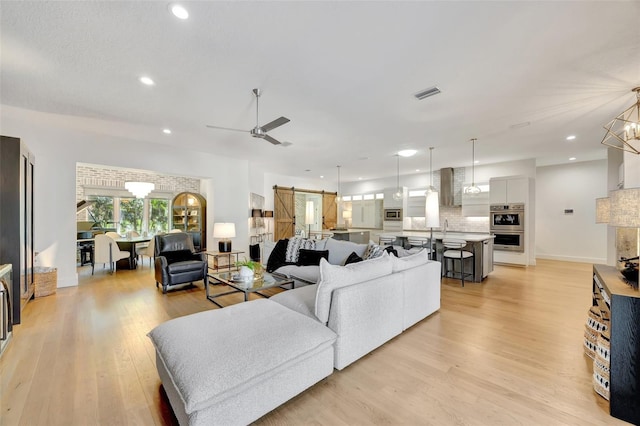 living room with a barn door, ceiling fan with notable chandelier, and light wood-type flooring