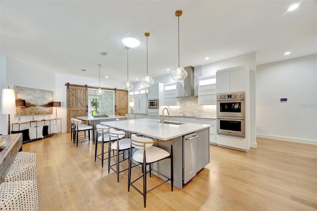 kitchen with wall chimney exhaust hood, a barn door, light hardwood / wood-style flooring, pendant lighting, and white cabinets