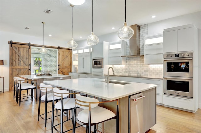 kitchen featuring a large island with sink, hanging light fixtures, a barn door, white cabinetry, and stainless steel appliances