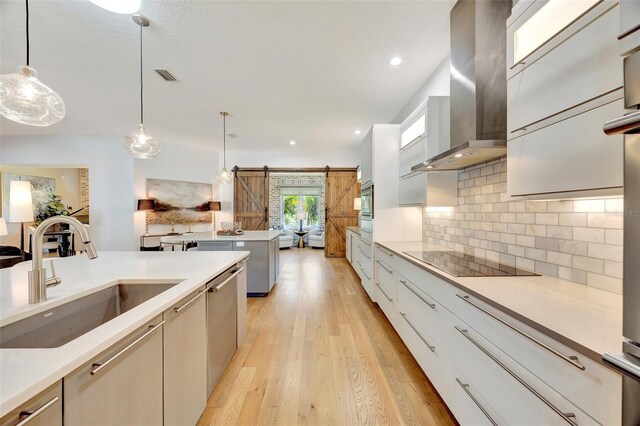 kitchen with sink, wall chimney exhaust hood, a barn door, pendant lighting, and light hardwood / wood-style floors