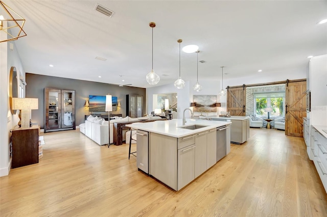 kitchen with sink, a barn door, decorative light fixtures, a center island with sink, and light hardwood / wood-style floors