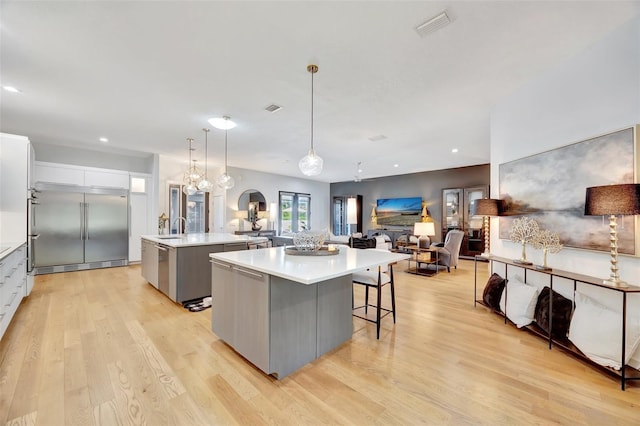 kitchen with light wood-type flooring, a spacious island, pendant lighting, built in refrigerator, and white cabinetry