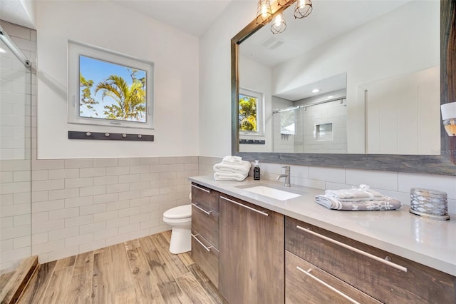 bathroom featuring hardwood / wood-style floors, vanity, toilet, tile walls, and a shower with shower door