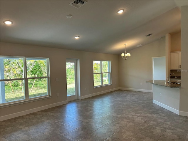 unfurnished living room featuring lofted ceiling, dark tile patterned floors, a notable chandelier, and sink