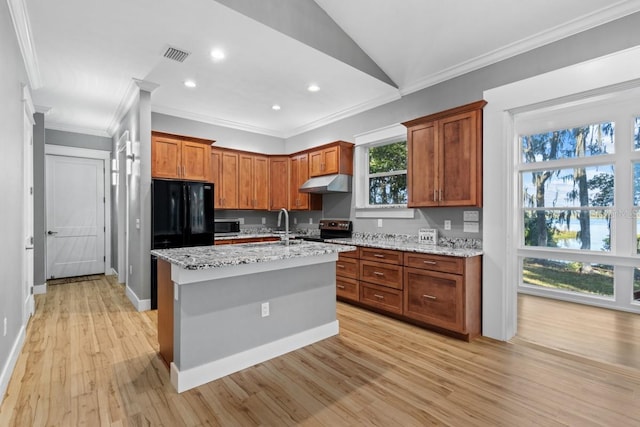 kitchen featuring black appliances, crown molding, light wood-type flooring, light stone countertops, and an island with sink