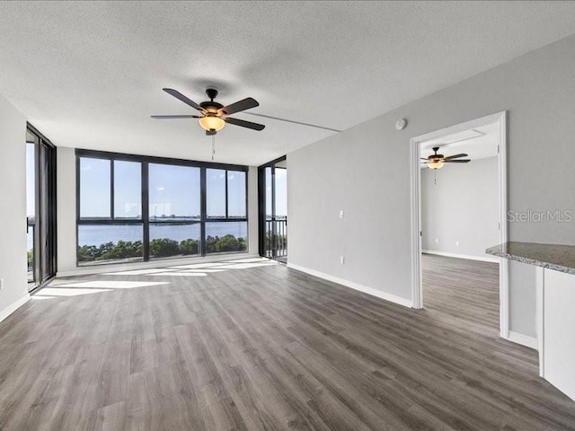 spare room featuring expansive windows, a textured ceiling, a water view, and dark hardwood / wood-style floors