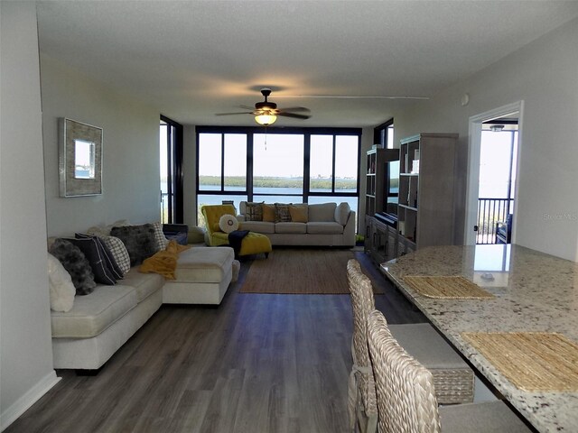 living room with a wealth of natural light, dark wood-type flooring, and ceiling fan