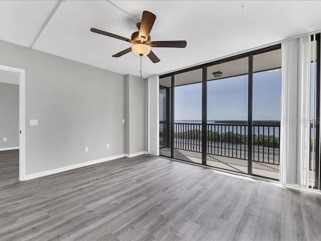 empty room with floor to ceiling windows, hardwood / wood-style floors, a water view, and ceiling fan