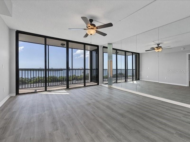 empty room featuring floor to ceiling windows, a water view, plenty of natural light, and ceiling fan