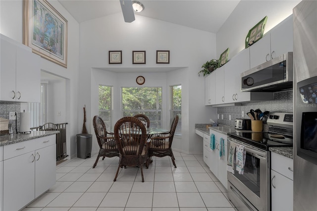 kitchen featuring white cabinets, appliances with stainless steel finishes, high vaulted ceiling, and dark stone countertops