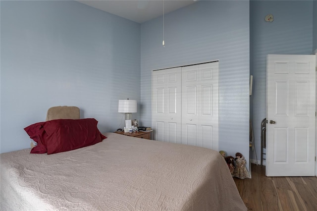 bedroom with hardwood / wood-style floors, a towering ceiling, and a closet