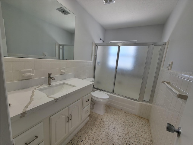 full bathroom featuring toilet, tile walls, vanity, and shower / bath combination with glass door