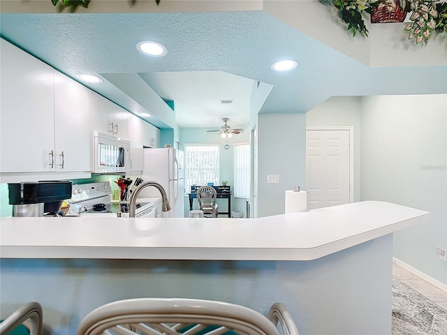 kitchen featuring ceiling fan, kitchen peninsula, a textured ceiling, white appliances, and white cabinets