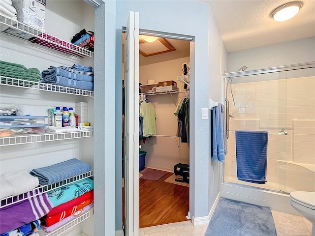 bathroom featuring tile patterned floors, a textured ceiling, an enclosed shower, and toilet