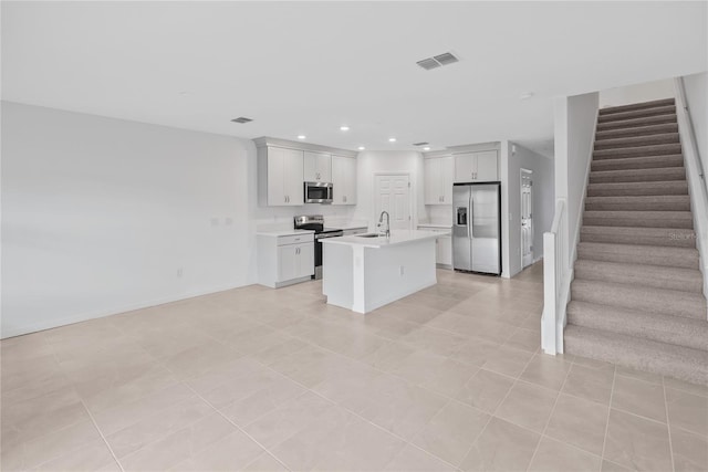 kitchen with a kitchen island with sink, white cabinets, sink, light tile patterned floors, and stainless steel appliances