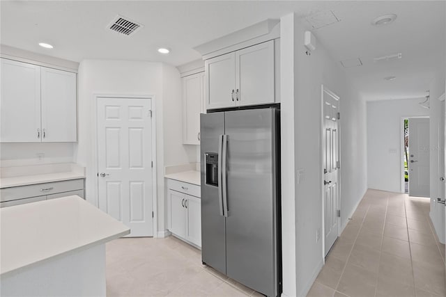 kitchen with stainless steel refrigerator with ice dispenser, light tile patterned floors, and white cabinetry