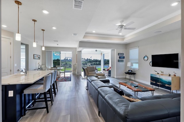 living room featuring hardwood / wood-style floors, sink, ornamental molding, a raised ceiling, and ceiling fan