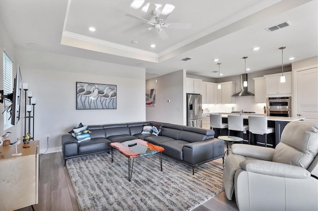 living room featuring ceiling fan, crown molding, a raised ceiling, and light wood-type flooring