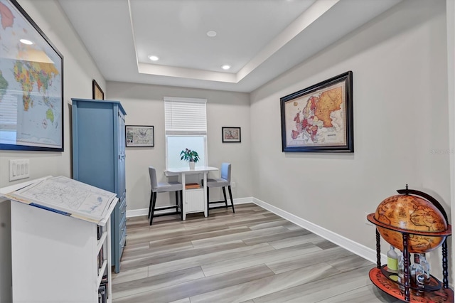 home office featuring a tray ceiling and light wood-type flooring