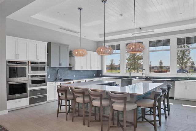 kitchen featuring a kitchen bar, stainless steel appliances, pendant lighting, and a raised ceiling