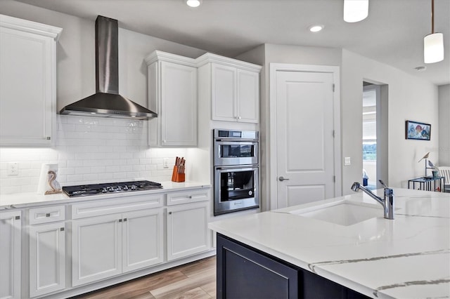 kitchen featuring pendant lighting, white cabinets, appliances with stainless steel finishes, wall chimney range hood, and decorative backsplash