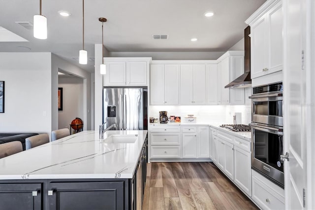 kitchen with appliances with stainless steel finishes, decorative light fixtures, white cabinetry, wall chimney range hood, and a breakfast bar area