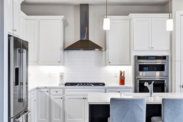 kitchen with hanging light fixtures, white cabinetry, wall chimney range hood, and appliances with stainless steel finishes