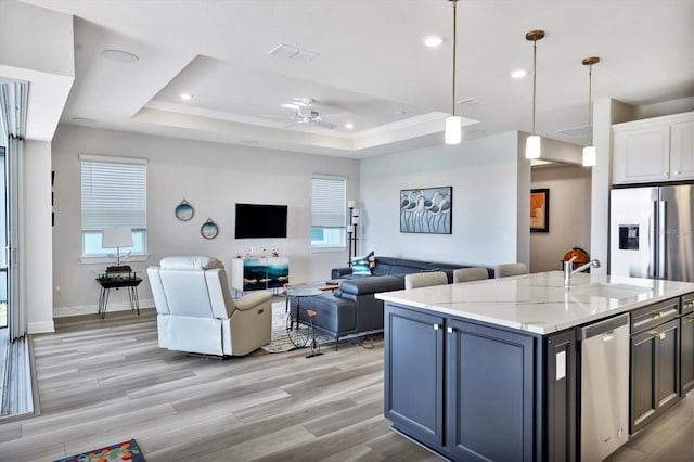 kitchen featuring light stone countertops, sink, decorative light fixtures, a raised ceiling, and a center island with sink